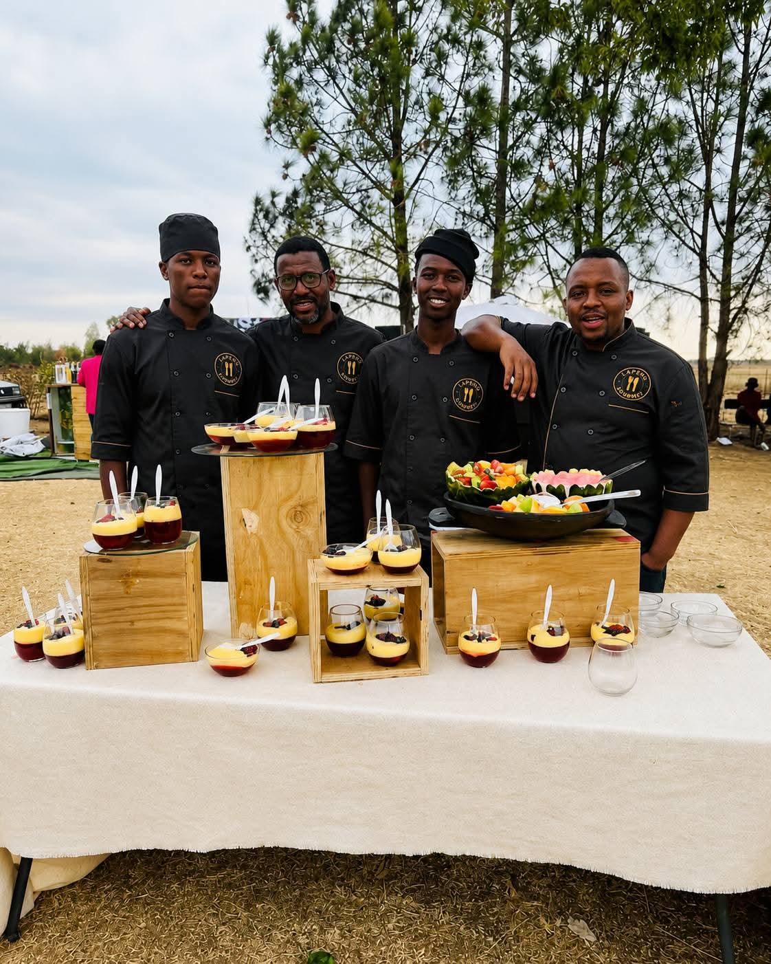 Lapeng Gourmet chefs beside a dessert and fruit station at an outdoor event
